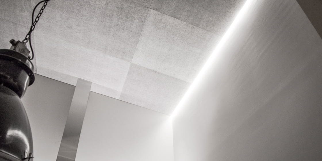 Modern minimalist interior with gray ceiling, built-in LED lighting at edges; industrial-style light fixture hangs from chain, smooth light walls