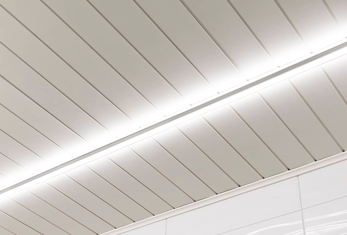 Lähikuva modernista kattorakenteesta, joka koostuu tyylikkäistä, rinnakkaisista valkoisista paneeleista ja kirkkaista lineaarisista LED-valoista. Puhdas ja minimalistinen muotoilu korostaa symmetriaa ja nykyaikaista tyyliä hyödyntämällä innovatiivista LED-teknologiaa, saatavilla LedStore.fi-sivustolta.