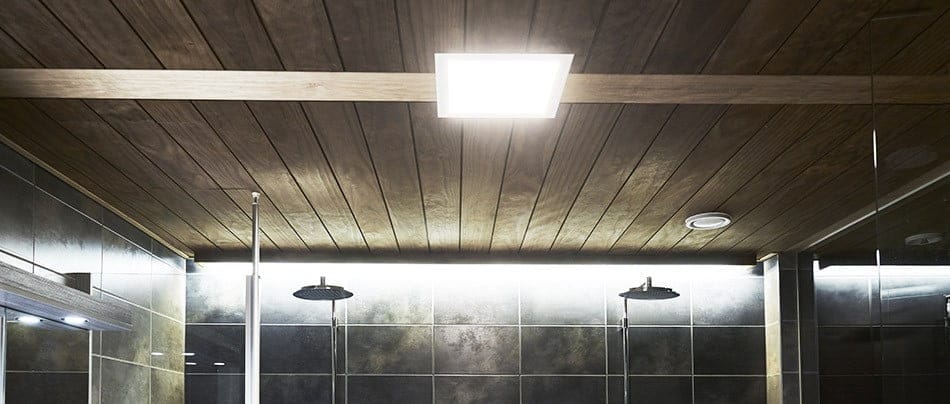 Katto näkymä modernista kylpyhuoneesta, jossa on puupaneelit ja kirkas LED-neliövalaisin. Alla kaksi mustaa suihkupäätä erottuvat tummaa laatoitettua seinää vasten, joka heijastaa valoa tyylikkäästi. Täydellinen ratkaisu LedStore.fi verkkokaupasta valitsemaasi kylpyhuonetyyliin.