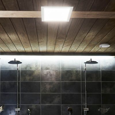 Wood panelled ceiling with recessed LED lights illuminating double shower heads on an elegant tiled bathroom wall.