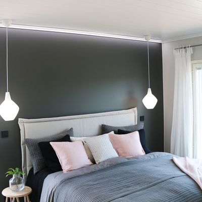 Modern bedroom with grey accent wall, pink-grey bedding, white pendant lights and small round wooden table with stylish LED lighting.