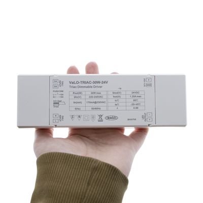 A person with the "VaLO-TRIAC-30W-24V" LED controller with specifications on a white surface, ideal for LED lighting systems.